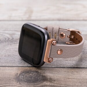 May include: A black smartwatch with a gray leather band and rose gold accents. The band has a buckle closure.