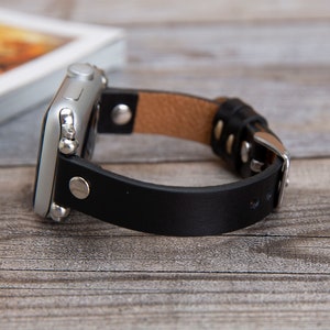 May include: A black leather watch band with a silver buckle and a silver Apple Watch.