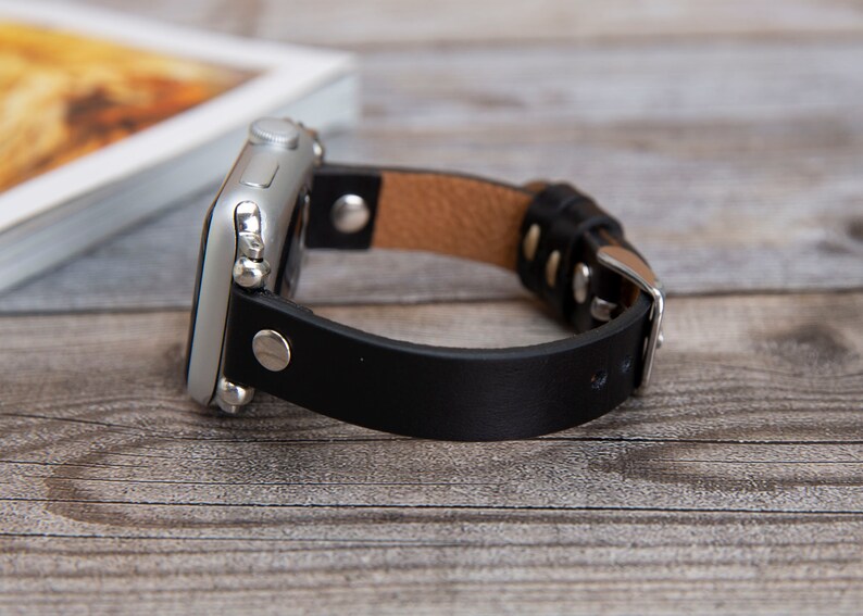 May include: A black leather watch band with a silver buckle and a silver Apple Watch.