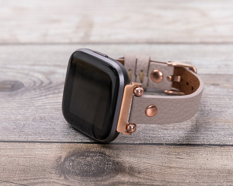 May include: A gray and black smartwatch with a rose gold band. The band is made of leather and has a textured finish.