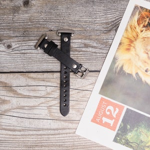 May include: Black leather watch band with silver hardware. The band is on a wooden surface.