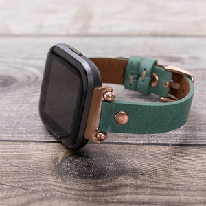 May include: A black smartwatch with a green leather band and rose gold accents. The band has a buckle closure.