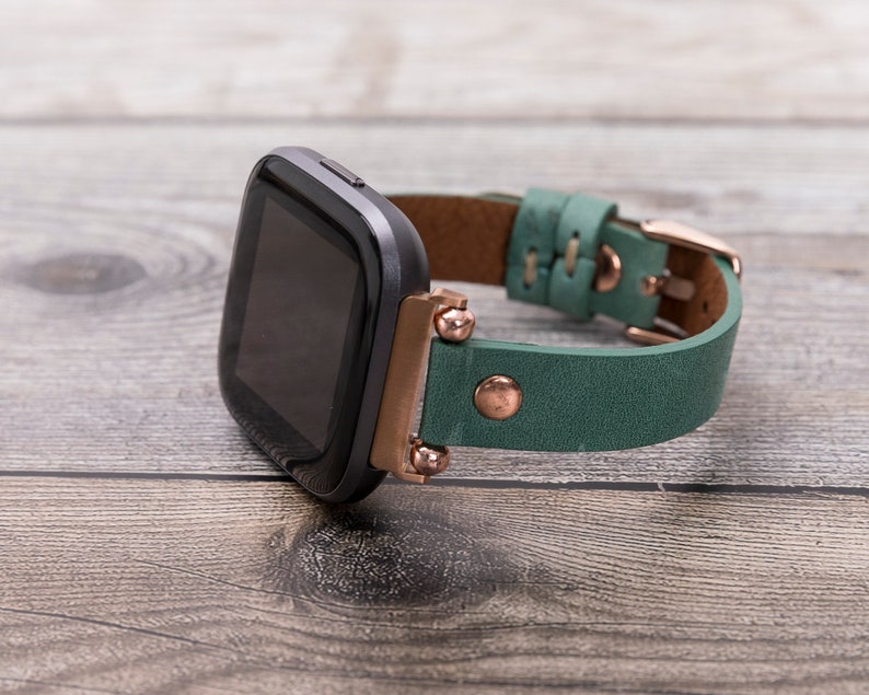 May include: A black smartwatch with a green leather band and rose gold accents. The band has a buckle closure.
