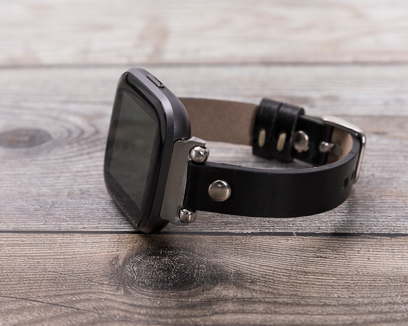 Puede incluir: Una correa de reloj de cuero negro con detalles plateados y una esfera de reloj cuadrada negra.
