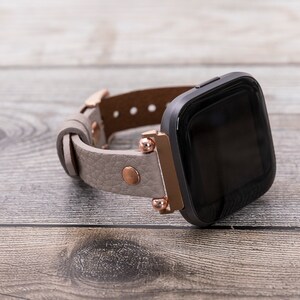 May include: A gray leather watch band with rose gold accents and a black smartwatch face.