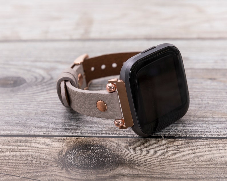May include: A gray leather watch band with rose gold accents and a black smartwatch face.