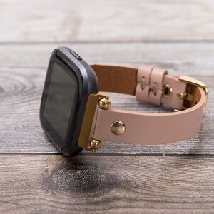 May include: A black and gold smartwatch with a pink leather band. The watch has a square face and a digital display.