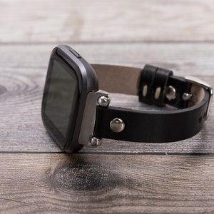 May include: A black leather watch band with silver accents and a black square watch face.
