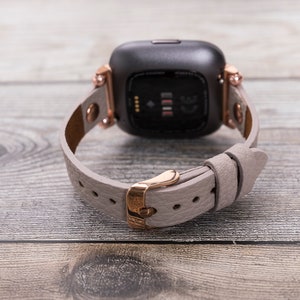May include: A rose gold smartwatch with a gray leather band. The watch face is black and has a digital display.