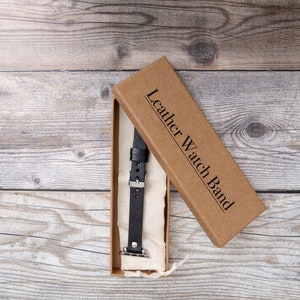 May include: A brown box with the text "Leather Watch Band" on the lid. The box is open and a black leather watch band is inside.