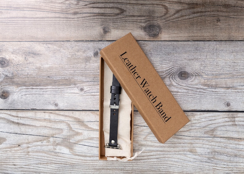 May include: A brown box with the text "Leather Watch Band" on the lid. The box is open and a black leather watch band is inside.