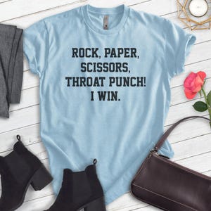 May include: Light blue t-shirt with the text "Rock, Paper, Scissors, Throat Punch! I Win."