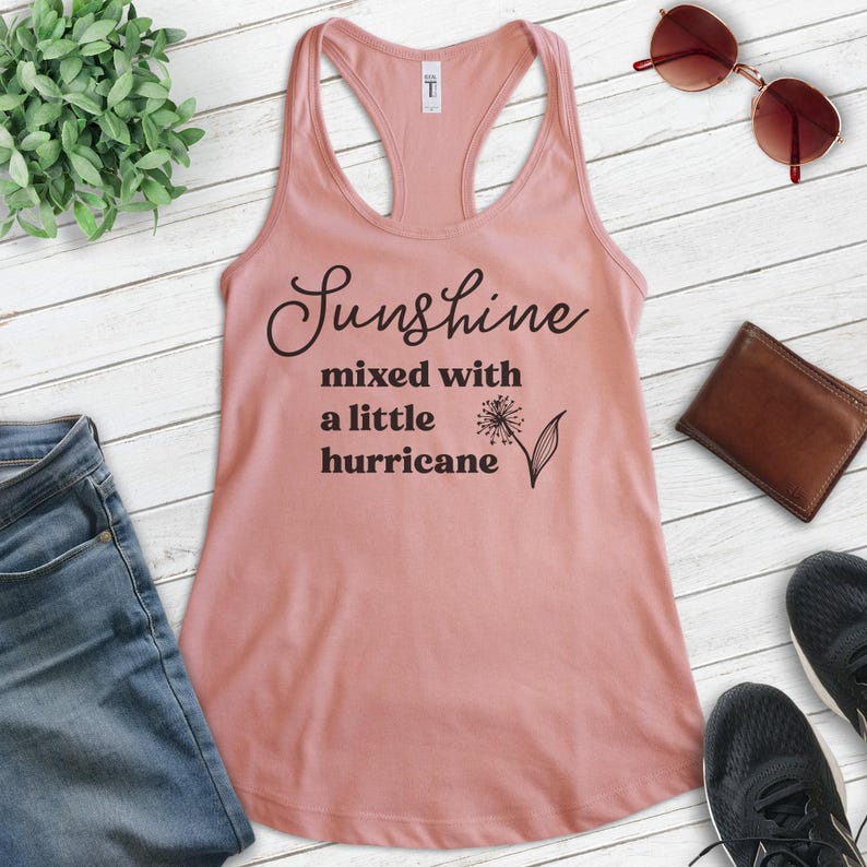 Puede incluir: Una camiseta de tirantes rosa con el texto "Sunshine mixed with a little hurricane" y un gr&aacute;fico de diente de le&oacute;n.