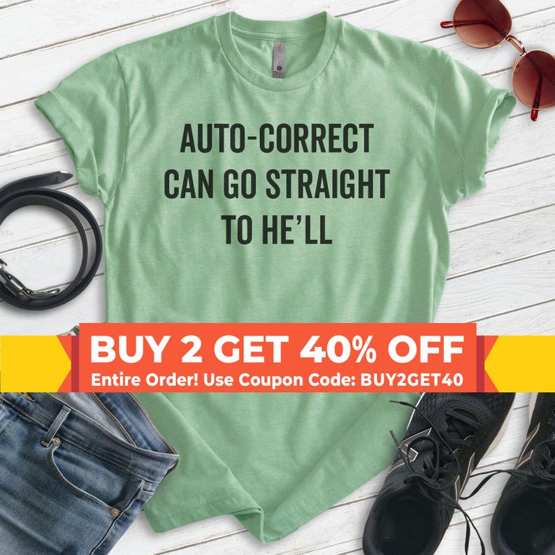May include: A light green t-shirt with the text "AUTO-CORRECT CAN GO STRAIGHT TO HE'LL" in black. The shirt is displayed with blue jeans, a black belt, sunglasses, and black sneakers.
