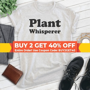 May include: A gray t-shirt with the text "Plant Whisperer" in black. The text is in a bold, retro font. A red and yellow banner at the bottom of the image reads "BUY 2 GET 40% OFF Entire Order! Use Coupon Code: BUY2GET40".