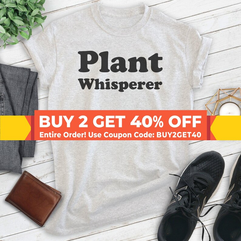 May include: A gray t-shirt with the text "Plant Whisperer" in black. The text is in a bold, retro font. A red and yellow banner at the bottom of the image reads "BUY 2 GET 40% OFF Entire Order! Use Coupon Code: BUY2GET40".