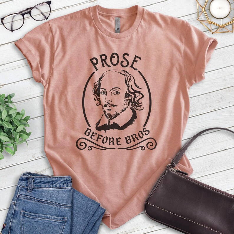 Puede incluir: Una camiseta rosa claro con un gr&aacute;fico negro del retrato de William Shakespeare en un c&iacute;rculo con el texto "Prose Before Bros" debajo.