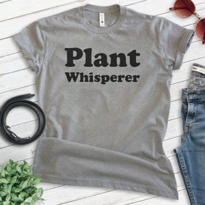 May include: Gray t-shirt with the text "Plant Whisperer" in black block letters.
