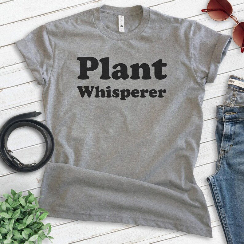 May include: Gray t-shirt with the text "Plant Whisperer" in black block letters.