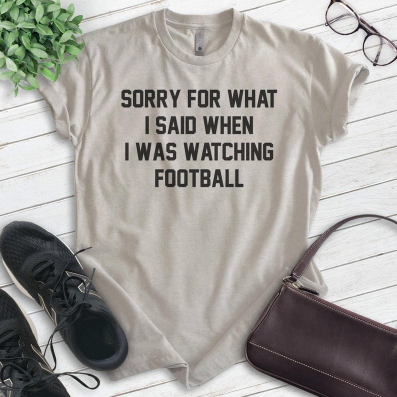 Pode incluir: Uma camiseta cinza claro com o texto "Desculpe pelo que eu disse quando estava assistindo futebol" impresso em preto.