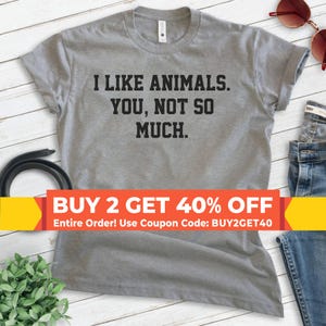 K&ouml;nnte beinhalten: Graues T-Shirt mit dem Text "Ich mag Tiere. Dich, nicht so sehr." Der Text ist in Schwarz. Ein gelbes und rotes Banner unten lautet "KAUFE 2, ERHALTE 40% RABATT Gesamte Bestellung! Nutze den Gutscheincode: BUY2GET40".