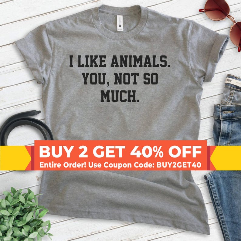 K&ouml;nnte beinhalten: Graues T-Shirt mit dem Text "Ich mag Tiere. Dich, nicht so sehr." Der Text ist in Schwarz. Ein gelbes und rotes Banner unten lautet "KAUFE 2, ERHALTE 40% RABATT Gesamte Bestellung! Nutze den Gutscheincode: BUY2GET40".