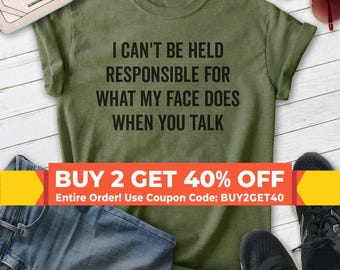 Puede incluir: Camiseta verde con el texto "No puedo ser considerado responsable de lo que mi cara hace cuando hablas". La camiseta está sobre una superficie de madera con vaqueros, gafas de sol y zapatillas.