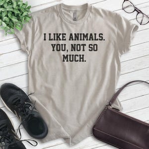K&ouml;nnte beinhalten: Ein hellgraues T-Shirt mit dem Text "Ich mag Tiere. Du, nicht so sehr." in Schwarz gedruckt.