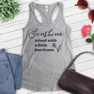 Puede incluir: Camiseta de tirantes gris con un gr&aacute;fico negro que dice "Sunshine mixed with a little hurricane" y un peque&ntilde;o gr&aacute;fico de diente de le&oacute;n.