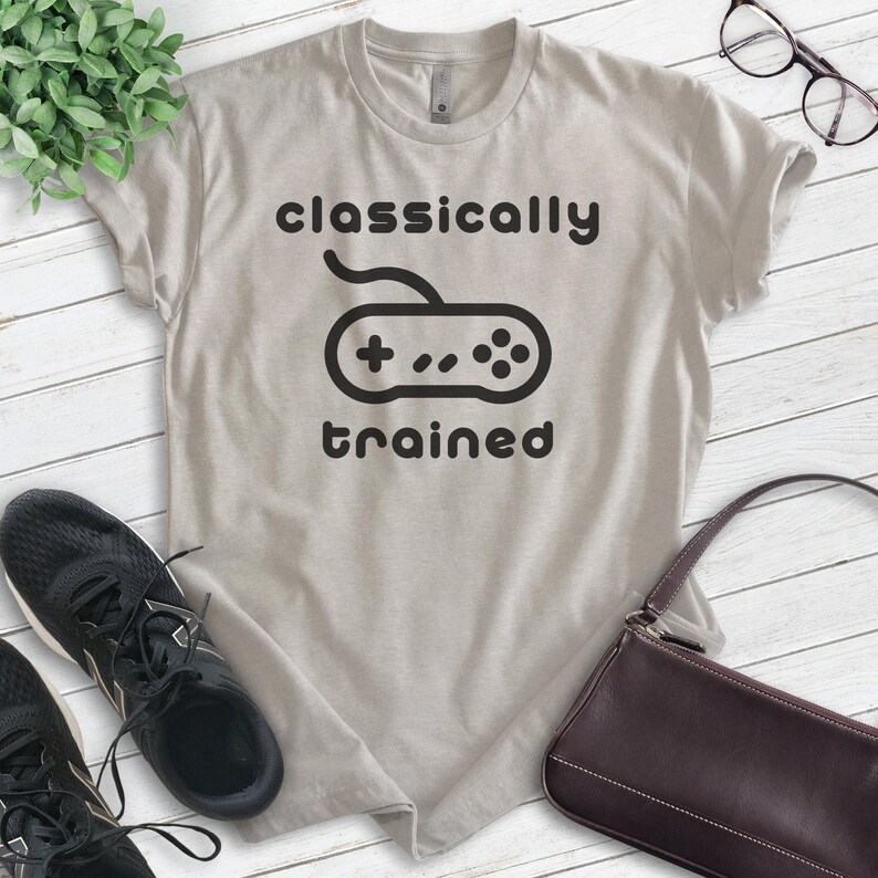 May include: A light gray t-shirt with the text "classically trained" and a black and white illustration of a video game controller.