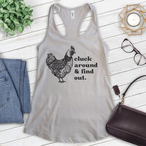Pu&ograve; includere: Un top a canotta grigio con un'illustrazione nera di una gallina e il testo "cluck around & find out."