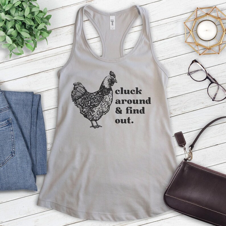 Pu&ograve; includere: Un top a canotta grigio con un'illustrazione nera di una gallina e il testo "cluck around & find out."
