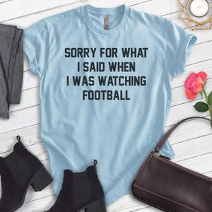 Pode incluir: Camiseta azul claro com o texto "Desculpe pelo que eu disse quando estava assistindo futebol".
