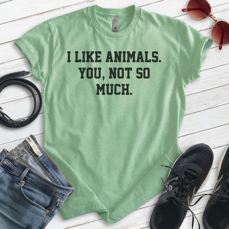 K&ouml;nnte beinhalten: Ein hellgr&uuml;nes T-Shirt mit dem Text "Ich mag Tiere. Du, nicht so sehr." in Schwarz gedruckt.