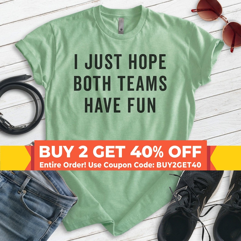 May include: A light green t-shirt with the text "I JUST HOPE BOTH TEAMS HAVE FUN" printed in black. The shirt has a crew neck and short sleeves. A banner at the bottom of the image reads "BUY 2 GET 40% OFF Entire Order! Use Coupon Code: BUY2GET40".
