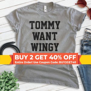 May include: A heather gray t-shirt with the words "TOMMY WANT WINGY" printed in bold black letters. The shirt has a crew neck and short sleeves. A banner at the bottom reads "BUY 2 GET 40% OFF".