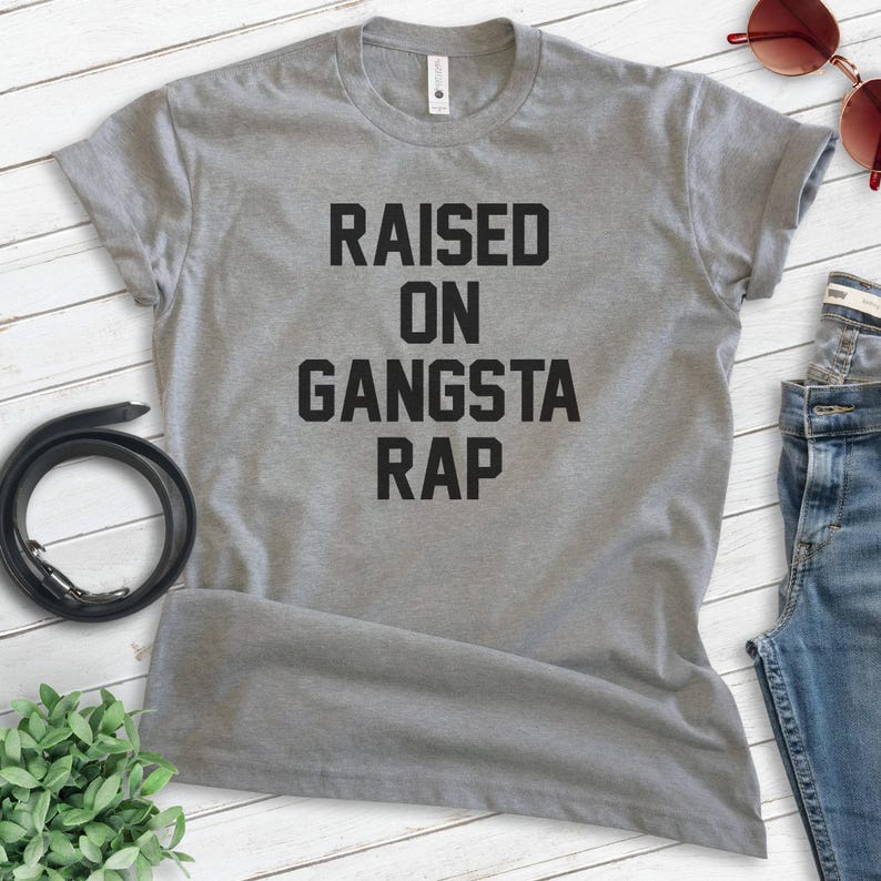 May include: Gray t-shirt with black text that reads "RAISED ON GANGSTA RAP".