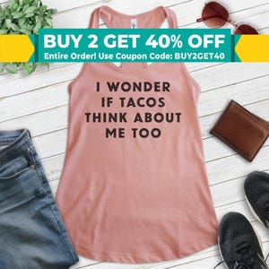 Może przedstawiać: R&oacute;żowy top na ramiączkach z nadrukiem "I wonder if tacos think about me too" w kolorze czarnym. Top leży na białym drewnianym tle z okularami przeciwsłonecznymi, brązowym portfelem i parą czarnych but&oacute;w.