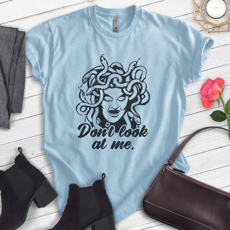 Pu&ograve; includere: T-shirt azzurra con grafica nera di Medusa e la scritta "Don't look at me". Il design presenta il volto di una donna con serpenti. Questa maglietta casual &egrave; realizzata in tessuto morbido.