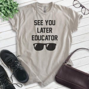 May include: A light gray t-shirt with the text "See You Later Educator" and a pair of sunglasses printed on it.