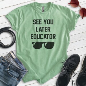 May include: A light green t-shirt with the text "See You Later Educator" in black lettering and a pair of black sunglasses.