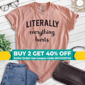 May include: A pink t-shirt with the text "LITERALLY everything hurts" in black. The shirt is on a wooden surface with a pair of jeans and a purse. The text "BUY 2 GET 40% OFF Entire Order! Use Coupon Code: BUY2GET40" is on a yellow and green banner.