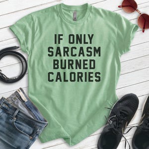 Puede incluir: Una camiseta verde claro con el texto "Si solo el sarcasmo quemara calor&iacute;as" impreso en negro.