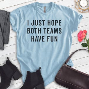 May include: Light blue t-shirt with the text "I just hope both teams have fun" printed in black.