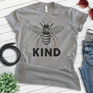 May include: Gray t-shirt with a black and white bee illustration and the word "KIND" printed in black.