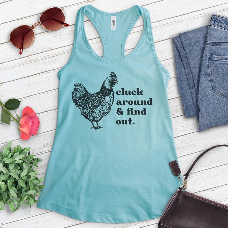 Pu&ograve; includere: Un top a canotta blu chiaro con una grafica nera di un pollo e il testo "cluck around & find out."