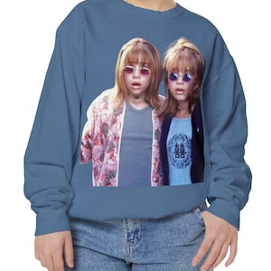 Puede incluir: Una sudadera azul con un gráfico de dos personas con gafas de sol. La persona de la izquierda lleva una chaqueta floral sobre una camisa gris, y la persona de la derecha lleva una chaqueta negra sobre una camisa azul con caracteres chinos.
