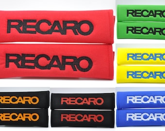 May include: Set of two seatbelt shoulder pads in various colors with the word "RECARO" embroidered on them. The pads are made of a soft, plush material and are designed to provide comfort and support while driving.