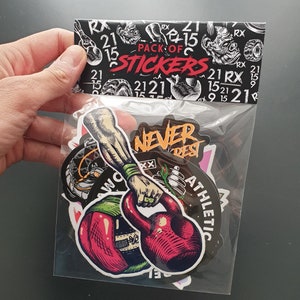 Puede incluir: Un paquete de pegatinas con una variedad de diseños, que incluyen una persona levantando una pesa rusa, una lata de aerosol y las palabras "Never Rest". Las pegatinas están sobre un fondo blanco y tienen un esquema de color negro y rojo.