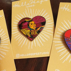 Puede incluir: Un pin de esmalte en forma de corazón con una ilustración colorida de una persona con la palabra "WORK" en el centro. El pin está en una tarjeta amarilla con el texto "Hello Peeps - Studio" y un icono de redes sociales.